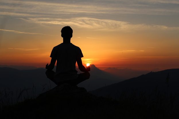 Man meditating on a mountain top at sunset