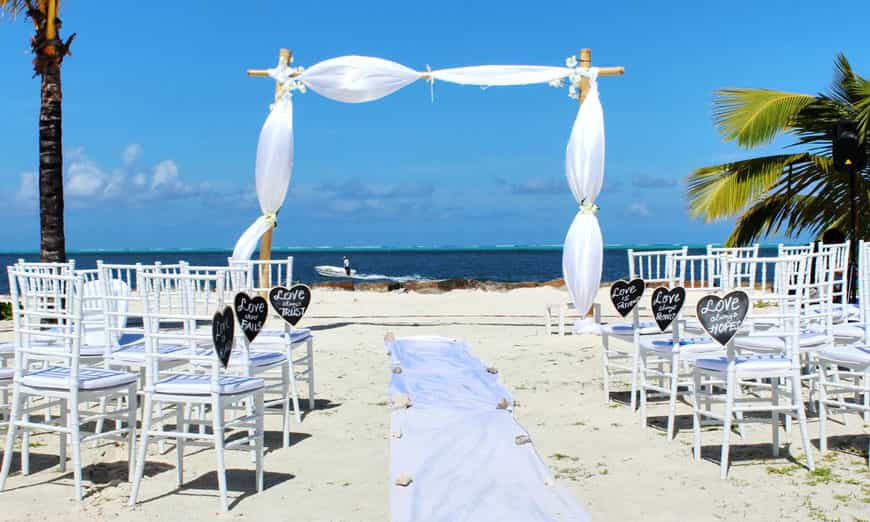 white archway and chairs set up for a wedding on the beach