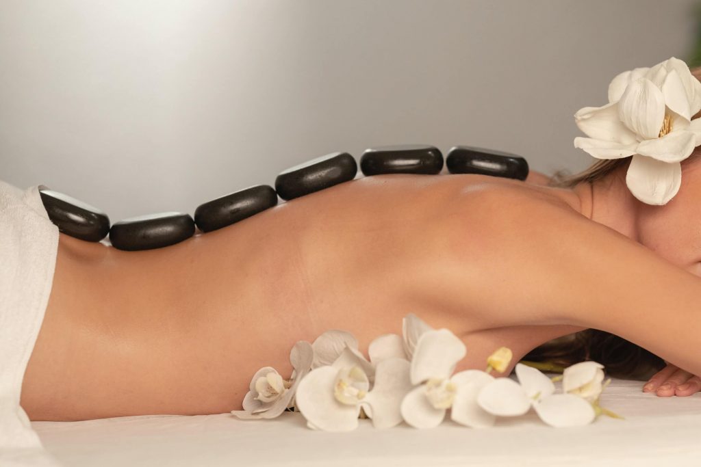 A woman lying on a bed with black rocks placed down her spine.